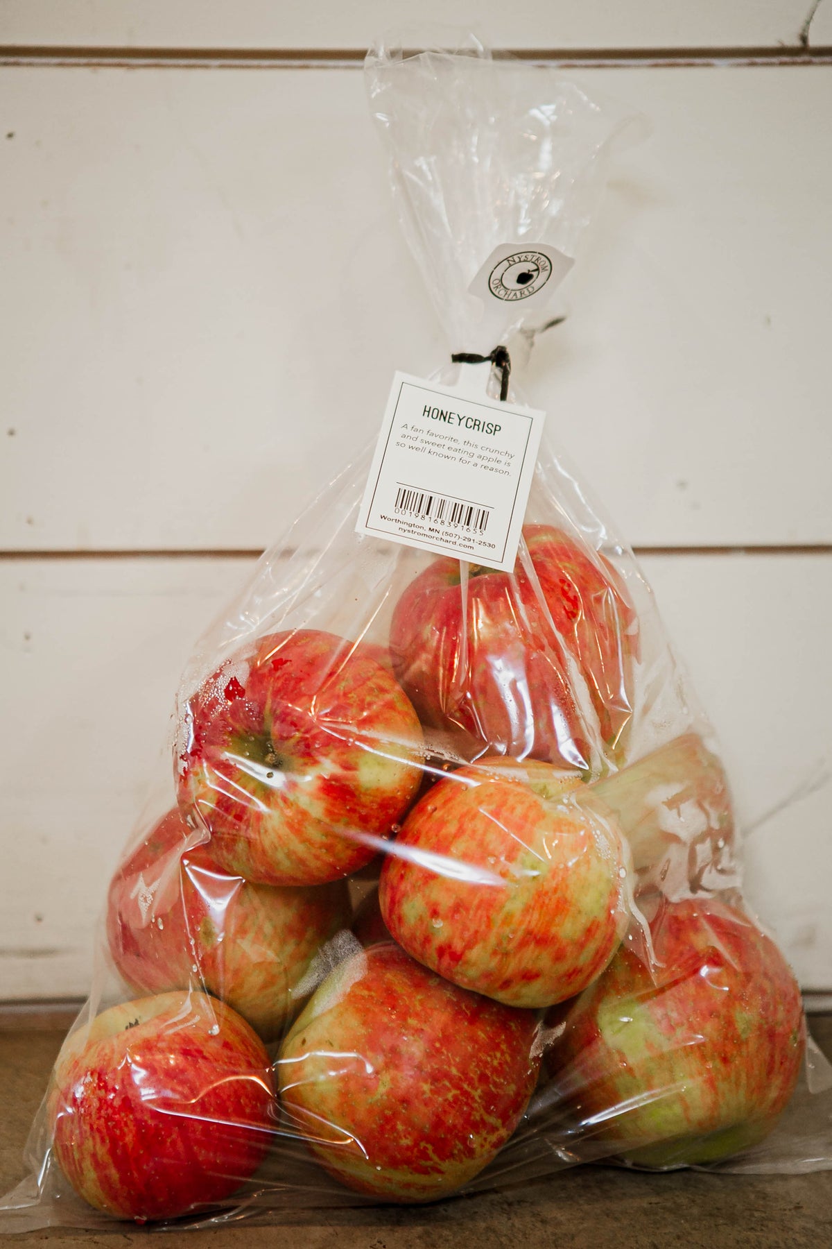 5 lb. Clear plastic bag of honeycrisp apples on a wooden surface with a white background. Picked in Nystrom Orchard in Worthington Minnesota.