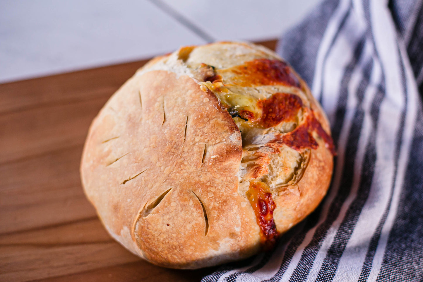 Artisan loaf of sourdough bread swirled with mozzarella cheese and fresh basil on a wooden cutting board with a black and white striped towel. Baked in the kitchen at Nystrom Orchard in Worthington Minnesota.
