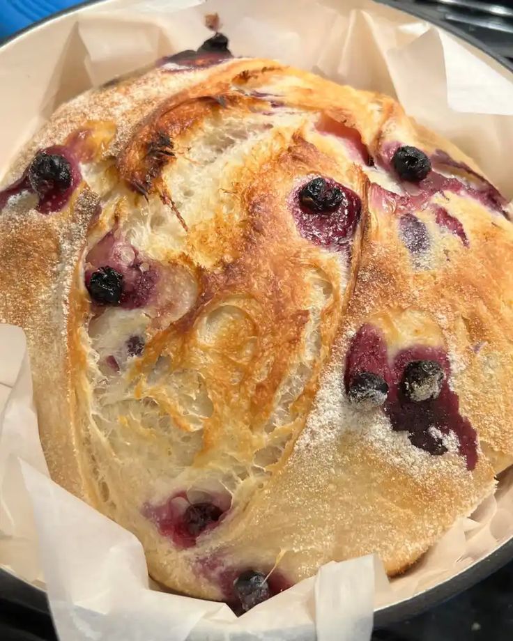 Rustic loaf of sourdough infused with blueberries and cream cheese in a blue dutch oven with parchment paper. Baked in the kitchen at Nystrom Orchard in Worthington Minnesota.