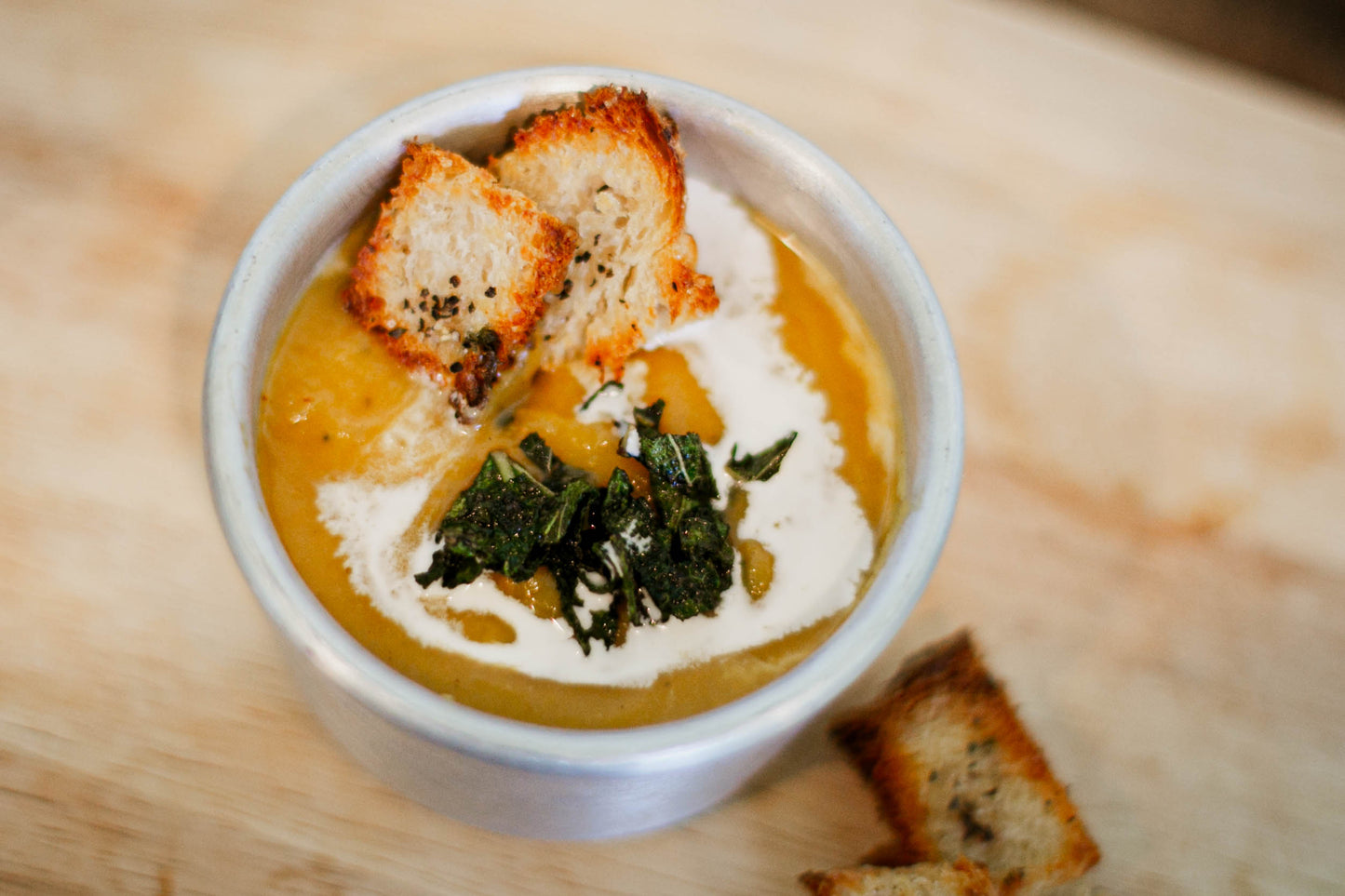 Bowl of butternut squash bisque with sourdough croutons and crispy sage on a wooden background. Made in the kitchen of Nystrom Orchard in Worthington Minnesota.