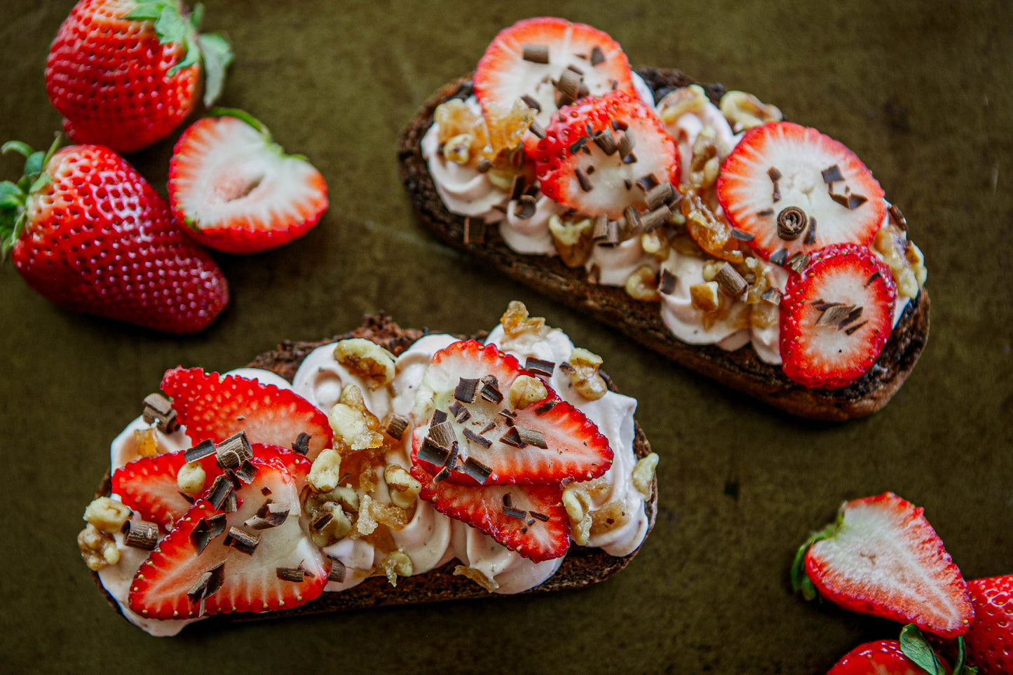Two slices of bread topped with whipped cream, strawberries, shaved chocolate and nuts on a dark surface with fresh strawberries beside. Prepared in the kitchen at Nystrom Orchard in Worthington Minnesota.