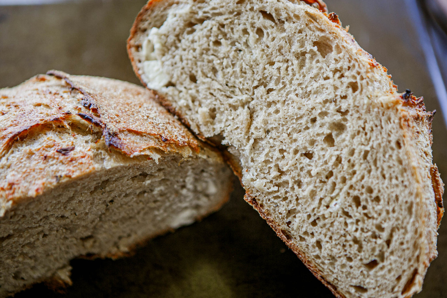 Close up of a rustic loaf of garlic rosemary sourdough bread cut in half so you can see the crumb on the inside on a dark surface. Baked in the kitchen at Nystrom Orchard in Worthington Minnesota.