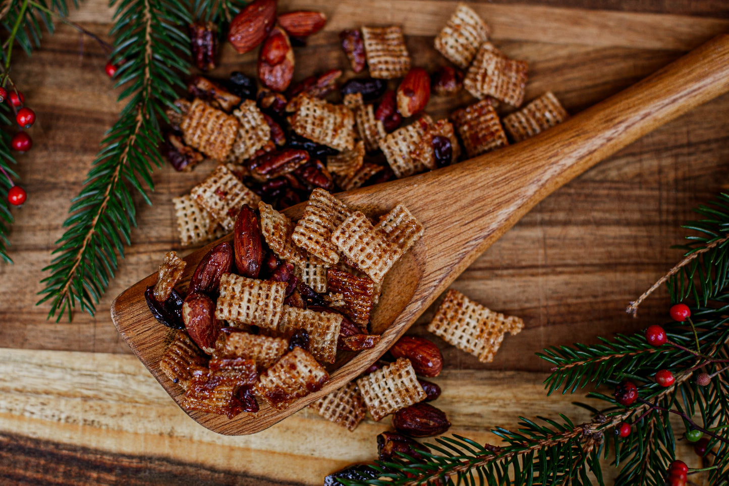 Wooden spoon filled with maple pecan snack mix on a wooden surface with Christmas decorations. Made in the kitchen at Nystrom Orchard in Worthington Minnesota.