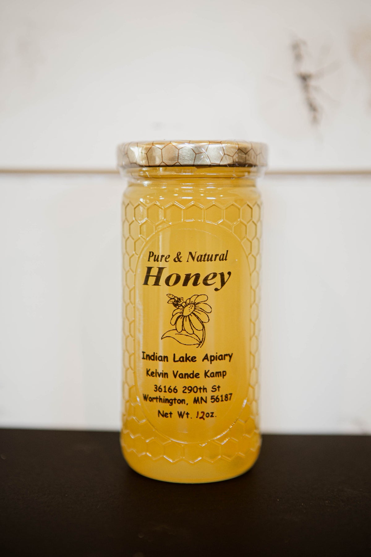 12 oz. honey in a glass jar on a dark surface with a white background. Honey sold by Nystrom Orchard in Worthington Minnesota.