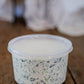 Container of creamy spinach dip in a clear container with a lid on a wooden surface and a blurred background. Made in the kitchen at Nystrom Orchard in Worthington Minnesota.