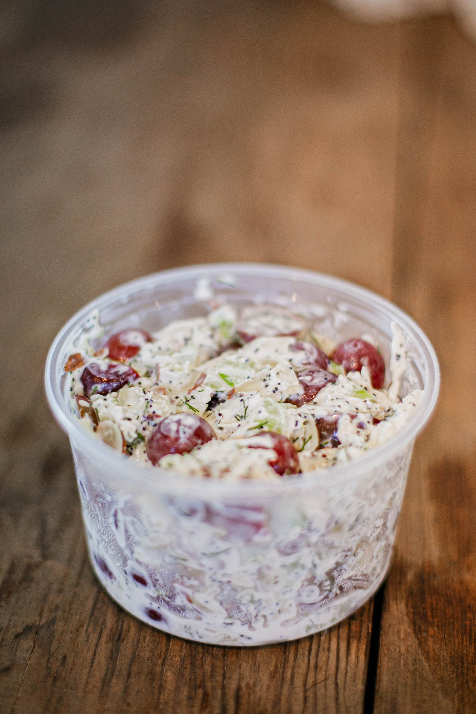 16 oz container of chicken salad containing grapes, celery, chicken, mayo and much more on a wooden surface.  Made in the kitchen of Nystrom Orchard in Worthington Minnesota.