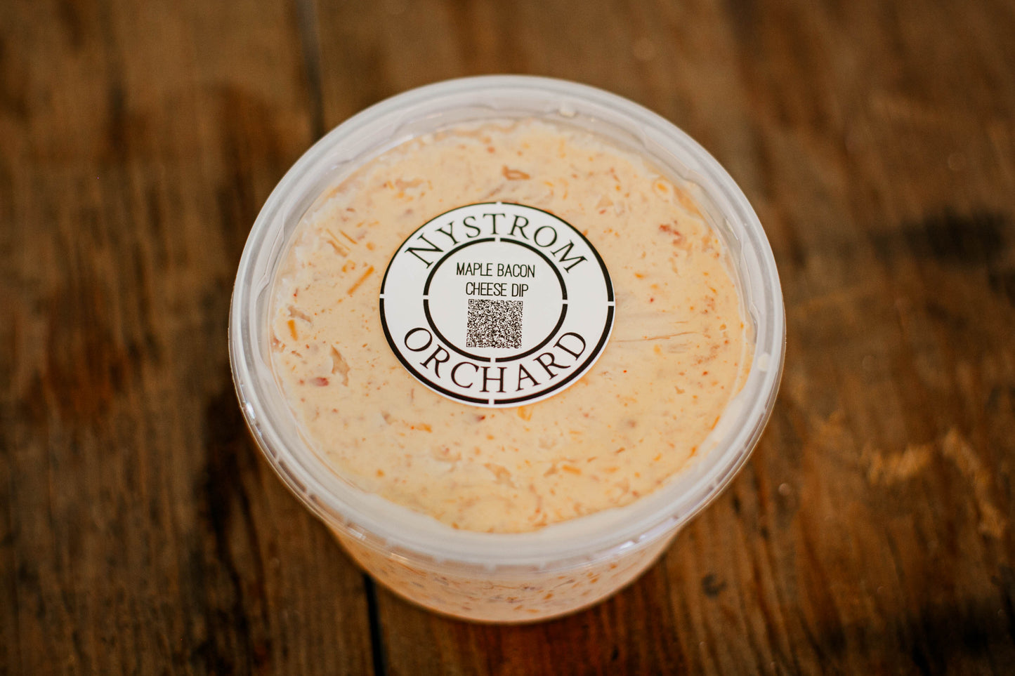 Container of maple bacon cheese dip with a lid on a wooden surface.  Made in the kitchen of Nystrom Orchard in Worthington Minnesota.