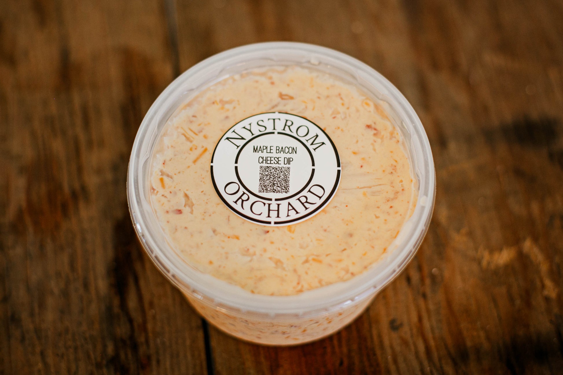 Container of maple bacon cheese dip with a lid on a wooden surface.  Made in the kitchen of Nystrom Orchard in Worthington Minnesota.