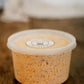 16 oz container of maple bacon cheese dip with a lid on a wooden surface with a blurry background.  Made in the kitchen of Nystrom Orchard in Worthington Minnesota.