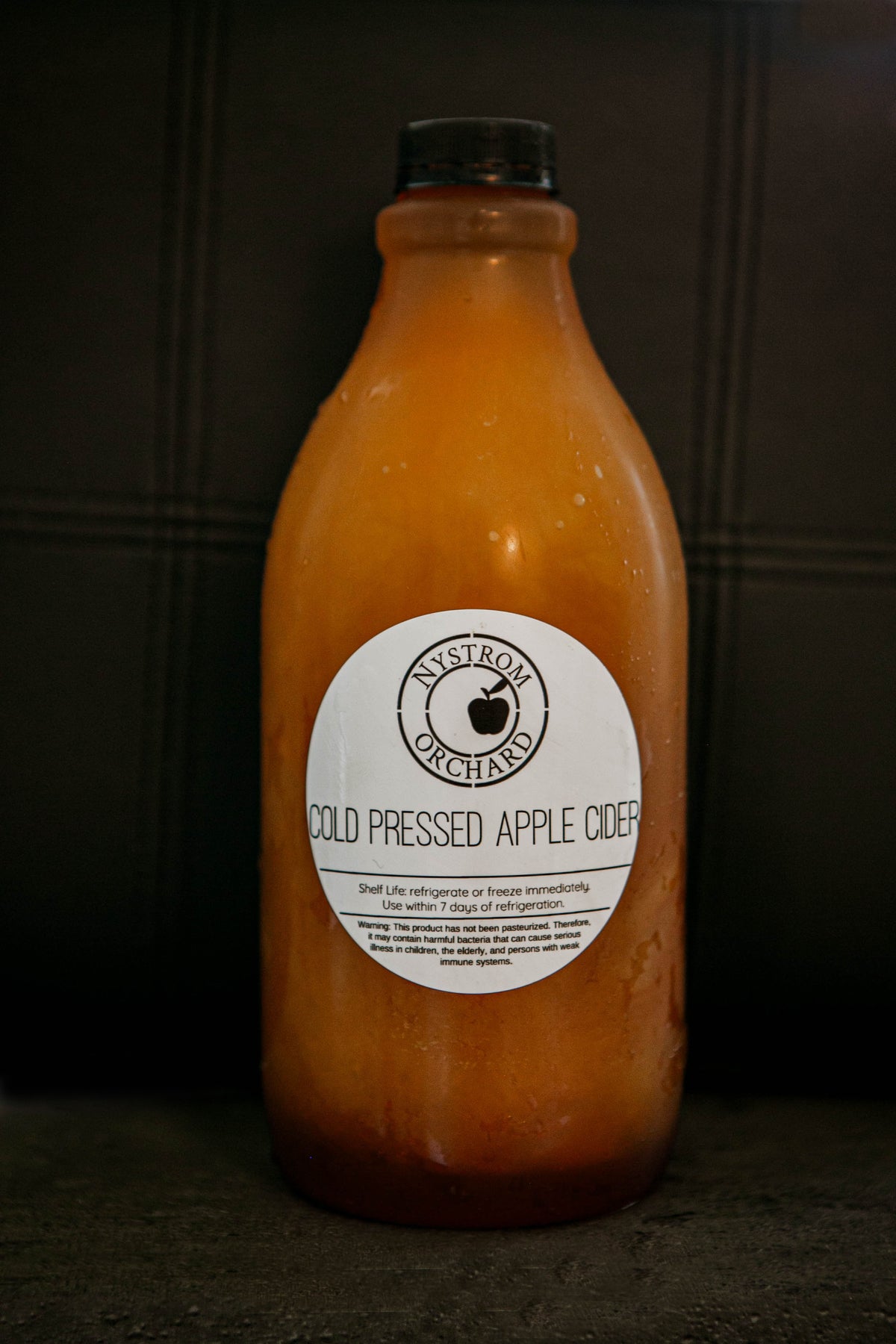 Large bottle of cold pressed cider on a dark background. Pressed in the kitchen of Nystrom Orchard in Worthington Minnesota.