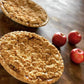 Two baked apple pies on a wooden surface with apples setting beside. Made by Nystrom Orchard in Worthington Minnesota.