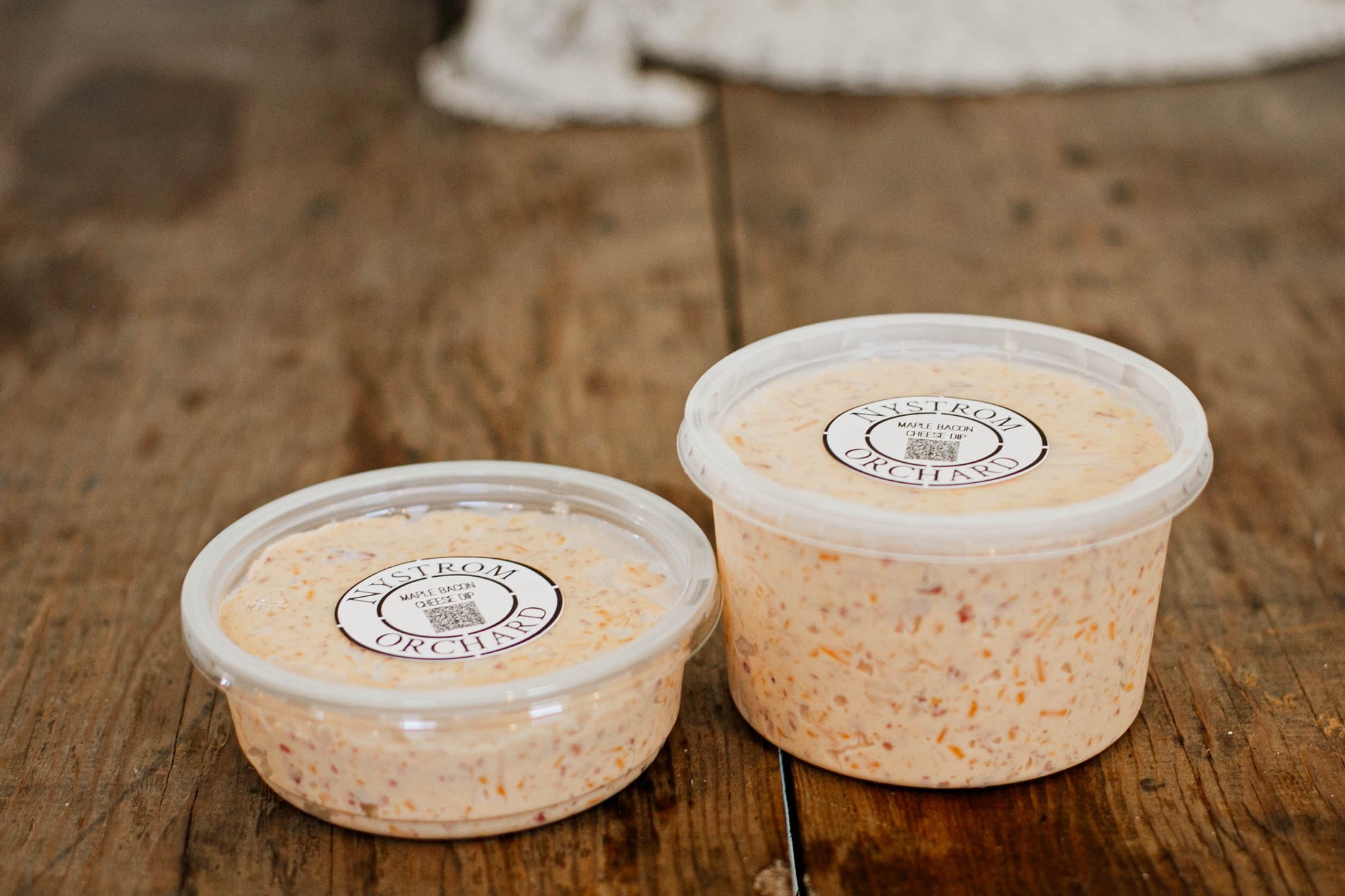 Both sizes of maple bacon cheese dip on a wooden surface. Made in the kitchen of Nystrom Orchard in Worthington Minnesota.