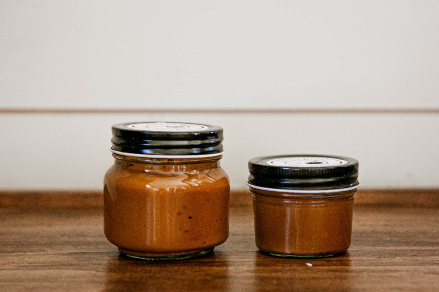 Two jars of salted caramel on a wooden surface. Made in the kitchen of Nystrom Orchard in Worthington Minnesota.