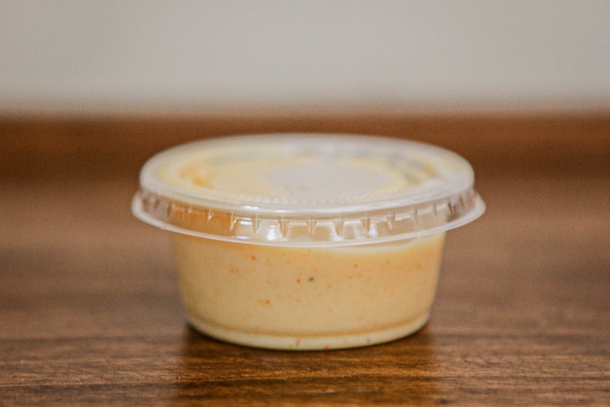 2 oz container with a lid of house made honey mustard on a wooden surface. Made in the kitchen of Nystrom Orchard in Worthington Minnesota.