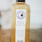 Bottle of house made apple cider vinegar on a wooden surface with a blurry background. Made in the kitchen of Nystrom Orchard in Worthington Minnesota.