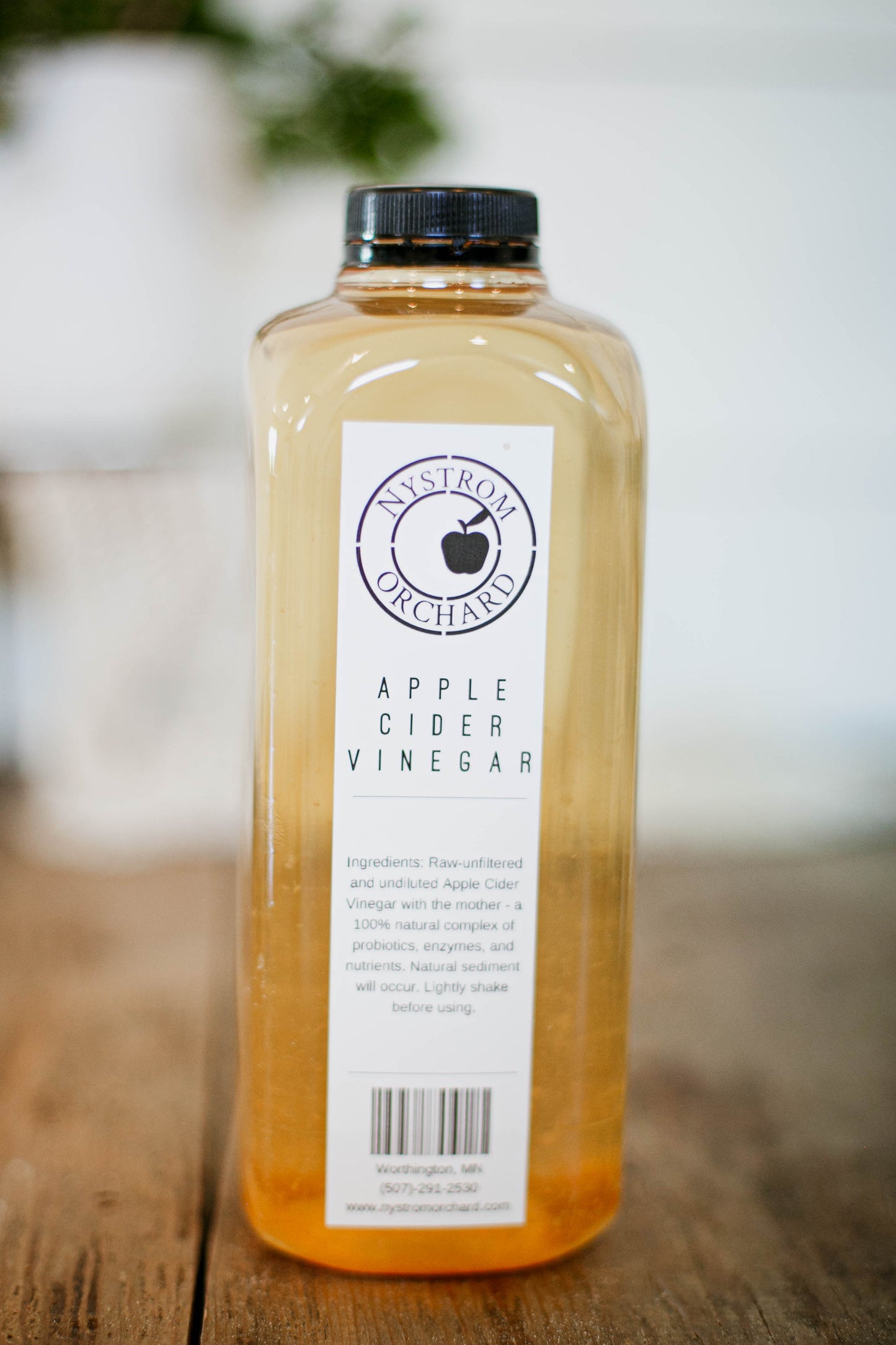 Bottle of house made apple cider vinegar on a wooden surface with a blurry background. Made in the kitchen of Nystrom Orchard in Worthington Minnesota.