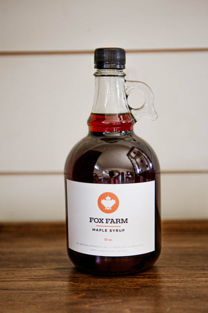 32 oz jug of maple syrup on a wooden surface with a white background. Sold by Nystrom Orchard in Worthington Minnesota.