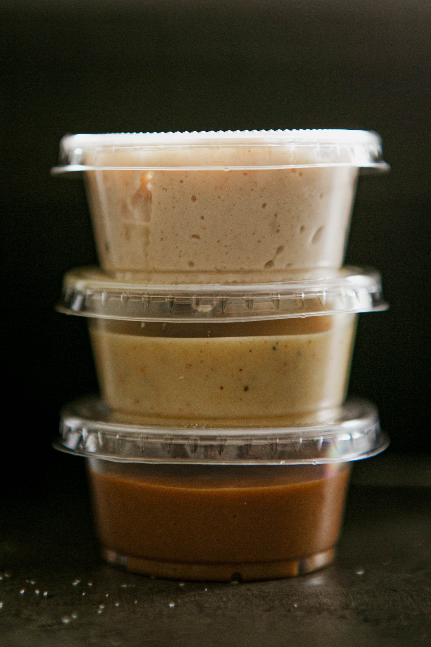 3 - 2 oz containers of house made dips stacked on top of each other on a black surface. Made in the kitchen of Nystrom Orchard in Worthington Minnesota. 