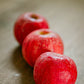 Three gala apples on a wooden table with a blurry background. Made in the kitchen of Nystrom Orchard in Worthington Minnesota.