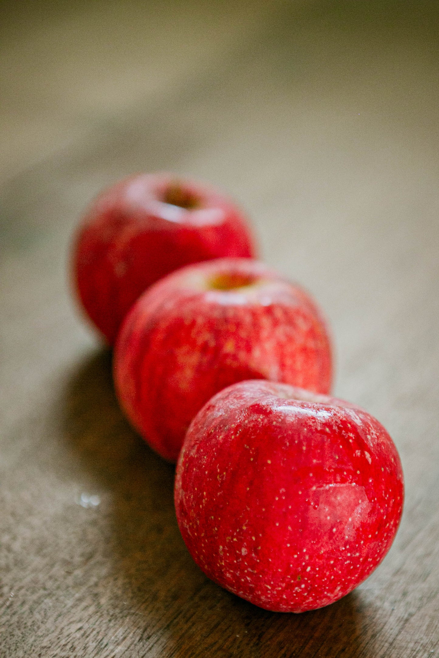 Three gala apples on a wooden table with a blurry background. Made in the kitchen of Nystrom Orchard in Worthington Minnesota.