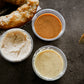 3- 2 oz containers of house made dips with a partial pretzel beside on a dark background. Made in the kitchen of Nystrom Orchard in Worthington Minnesota. 