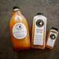 Three bottles of cold pressed cider on a textured surface, with varying sizes and labels indicating different types of cider. Made in the kitchen of Nystrom in Worthington Minnesota.