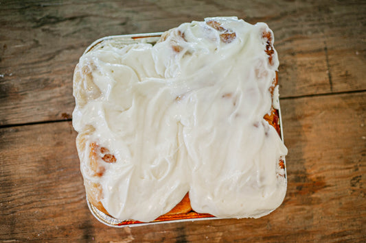 Four sourdough cinnamon rolls in a foil pan with cream cheese frosting on a wooden surface. Baked in the kitchen of Nystrom Orchard in Worthington Minnesota. 