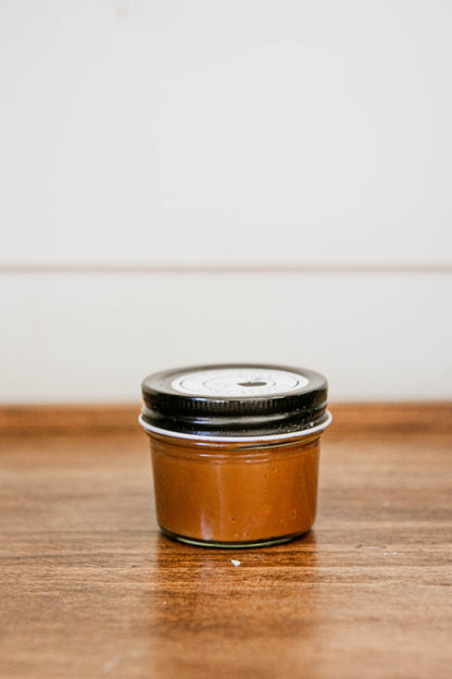 4 oz jar salted caramel with a black lid on a wooden surface. Made in the kitchen of Nystrom Orchard in Worthington Minnesota.