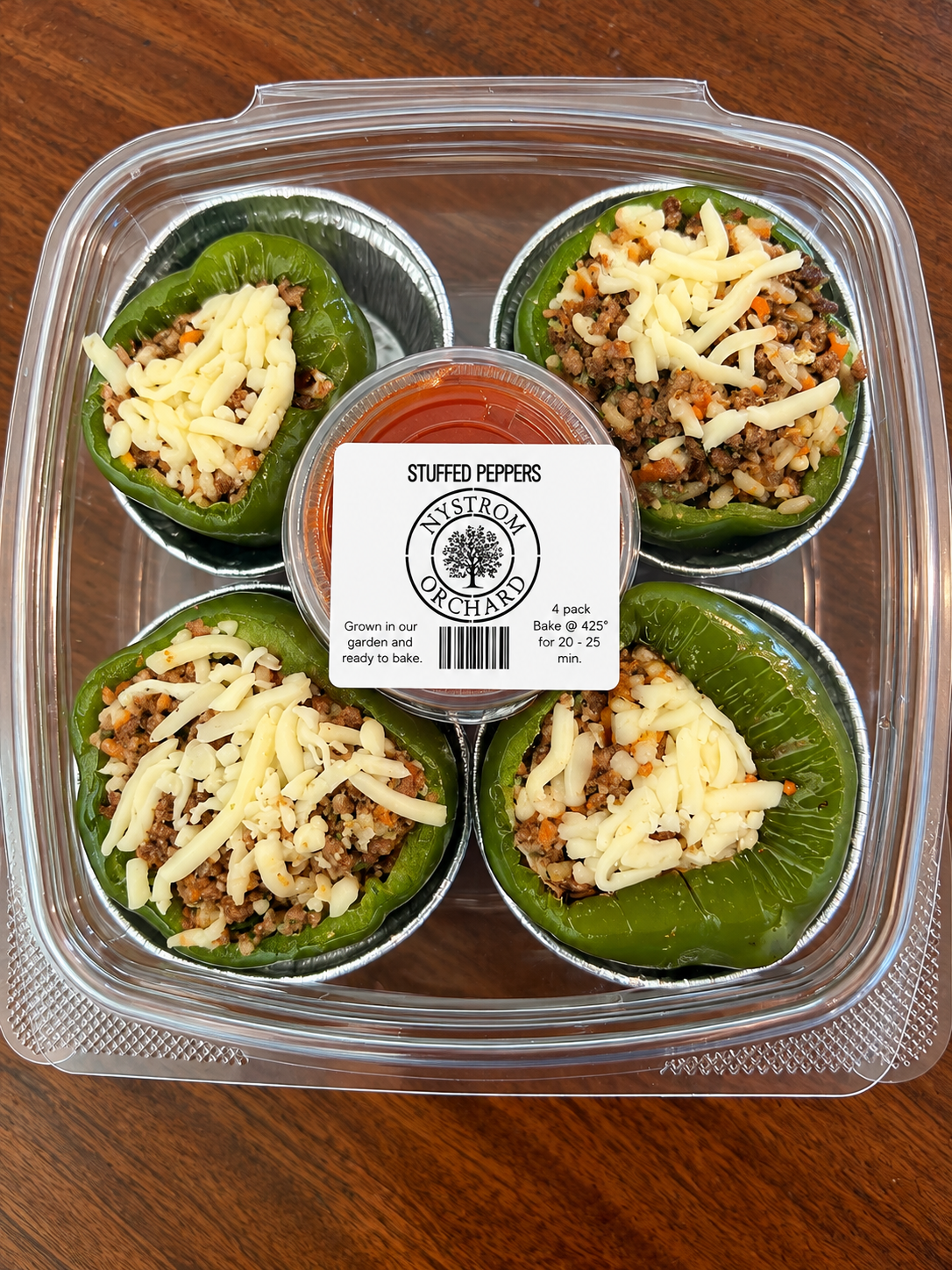 Plastic deli container with stuffed peppers and sauce labeled on a wooden surface. Made in the kitchen of Nystrom Orchard in Worthington Minnesota.