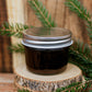 Jar of chocolate fudge sauce with a metal lid on a wooden stand with greenery. Made in the kitchen at Nystrom Orchard in Worthington Minnesota.