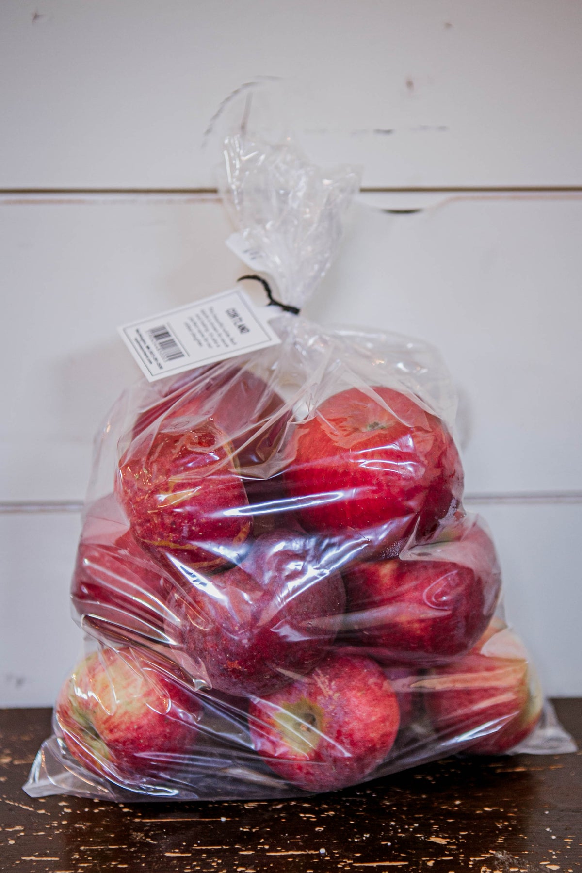 A clear plastic 5 lb bag of Cortland appleson a wooden table with a white background. Picked in Nystrom Orchard in Worthington Minnesota.