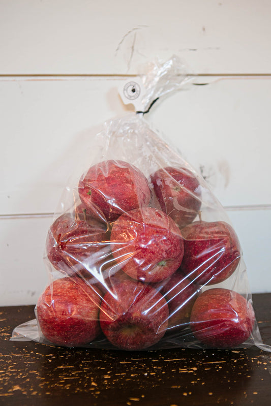 A plastic bag containing red Keepsake apples placed on a wooden surface with a white background. Picked in Nystrom Orchard in Worthington Minnesota.