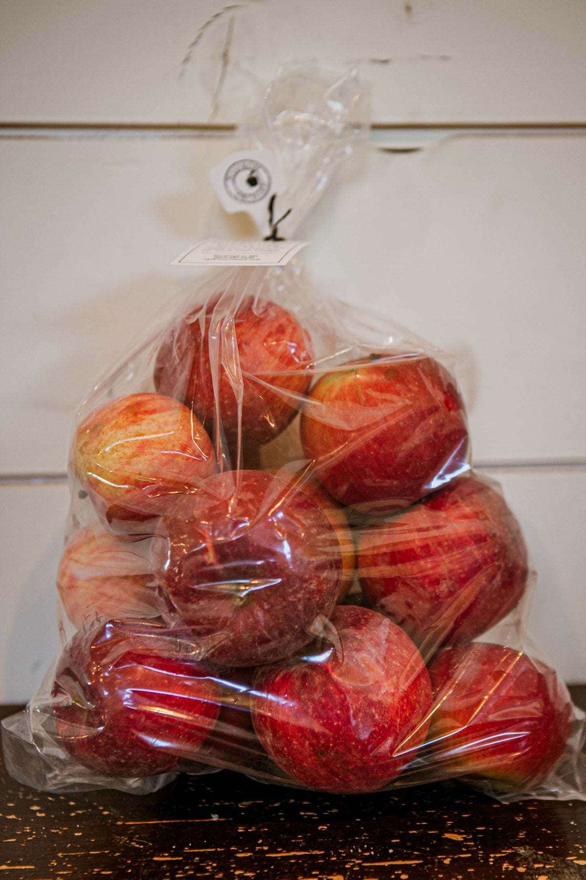 A clear 5lb plastic bag of Harlson apples on a wooden surface and a white background. Picked in Nystrom Orchard in Worthington Minnesota.