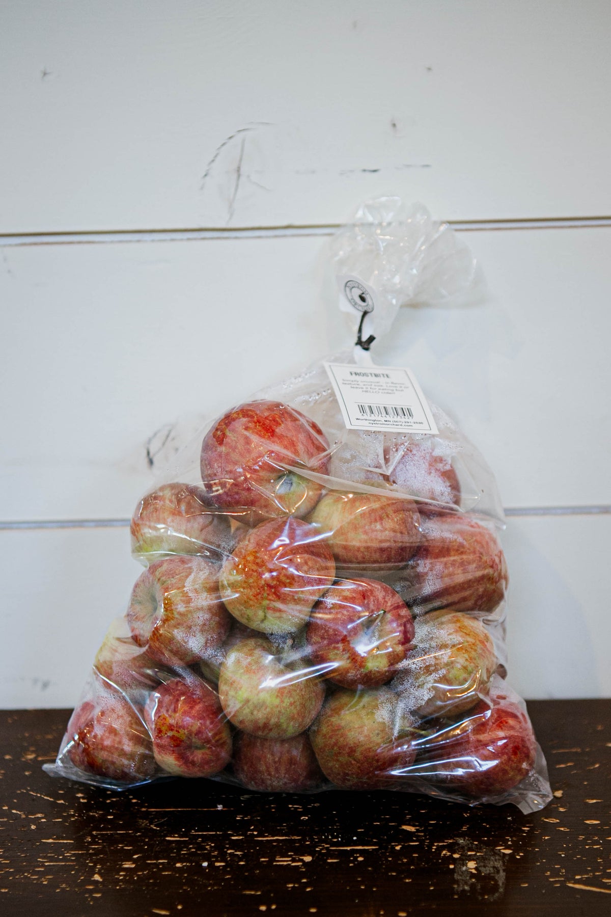 A clear plastic bag of apples of the variety frostbite on a wooden table with a white background. Picked in the orchard of Nystrom Orchard in Worthington Minnesota.