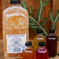 64 oz cold pressed cider with 4 bottles of cider syrup on a wooden surface with greenery and red berries. Made in the kitchen at Nystrom Orchard in Worthington Minnesota.
