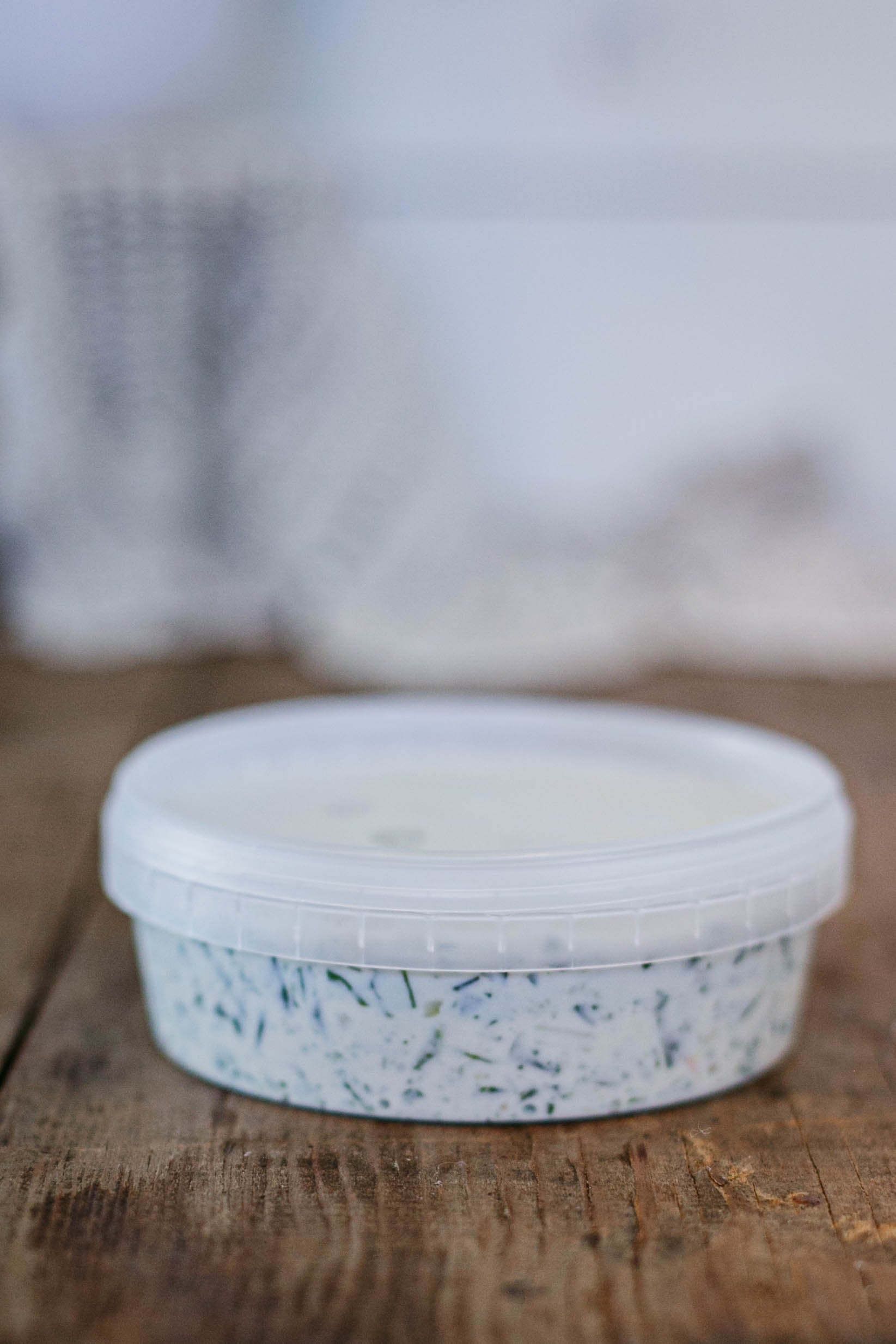 Container of spinach dip with a white lid on a wooden surface. Made in the kitchen of Nystrom Orchard in Worthington Minnesota.