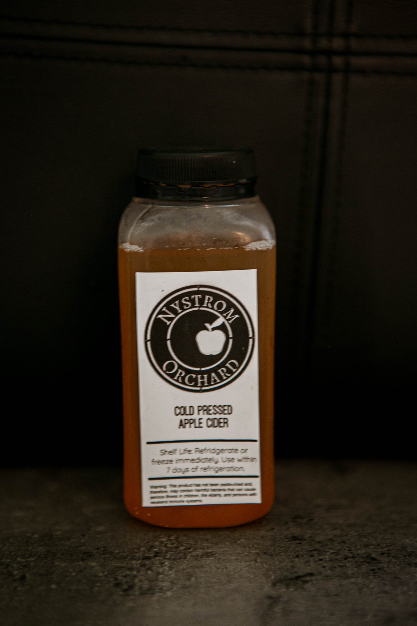 8 oz bottle of cold pressed cider with a dark background. Pressed in the kitchen of Nystrom Orchard in Worthington Minnesota.