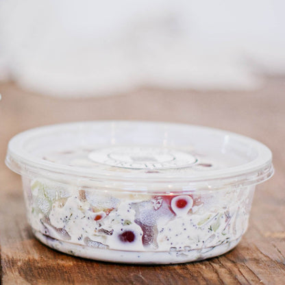 8 oz deli container with chicken salad and a lid on a wooden surface with a blurry background. Made in the kitchen of Nystrom Orchard in Worthington Minnesota.