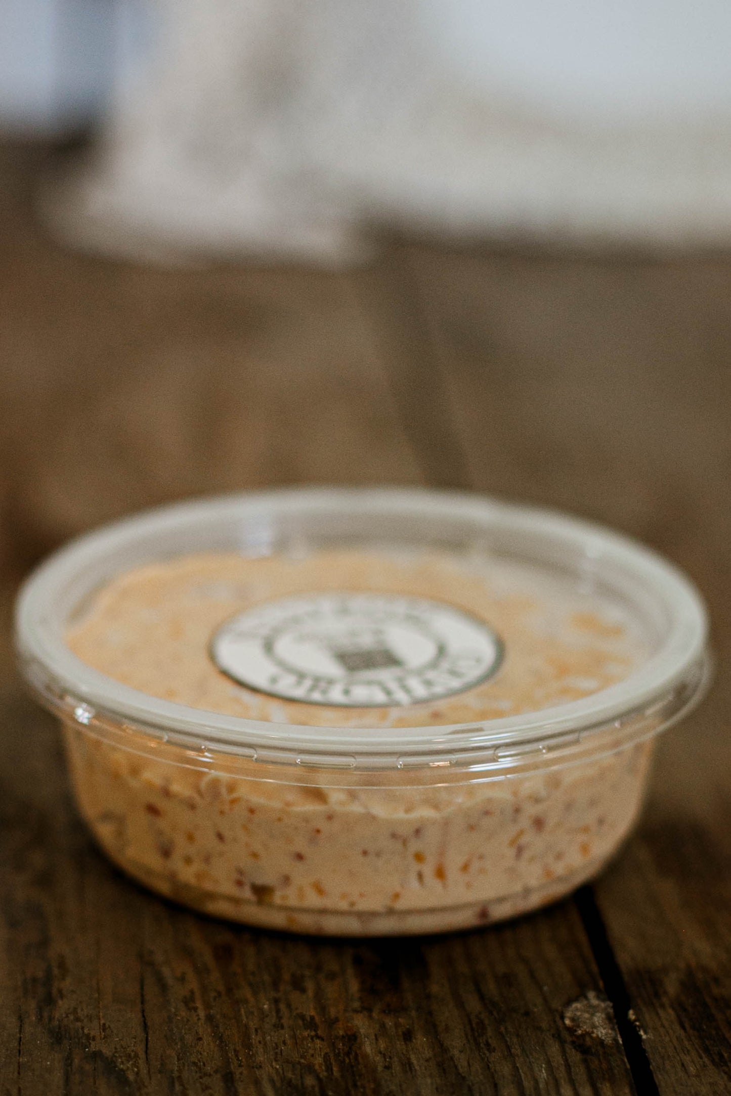 8 oz. container of maple bacon cheese dip with a lid on a wooden surface with a blurry background.  Made in the kitchen of Nystrom Orchard in Worthington Minnesota.
