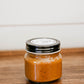8 oz jar salted caramel with a black lid on a wooden surface. Made in the kitchen of Nystrom Orchard in Worthington Minnesota.