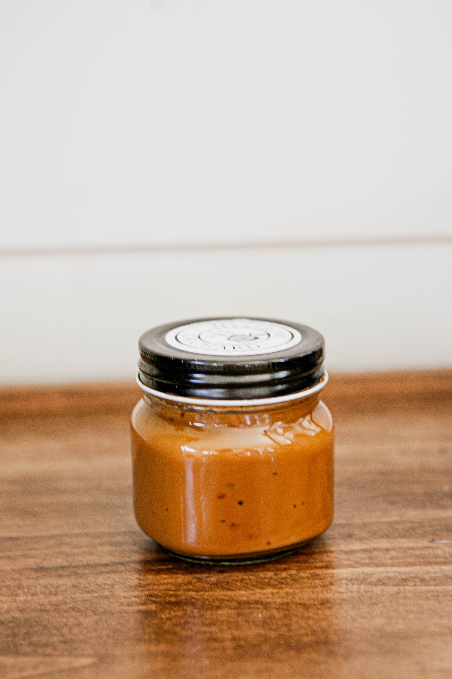 8 oz jar salted caramel with a black lid on a wooden surface. Made in the kitchen of Nystrom Orchard in Worthington Minnesota.