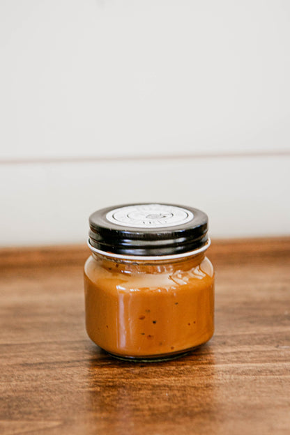 8 oz jar salted caramel with a black lid on a wooden surface. Made in the kitchen of Nystrom Orchard in Worthington Minnesota.