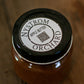 Jar of Nystrom Orchard apple butter with a black lid on a wooden surface. Made in the kitchen of Nystrom Orchard in Worthington Minnesota.