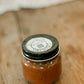 Jar of Apple Butter with a black lid on a wooden surface. Made in the kitchen of Nystrom Orchard in Worthington Minnesota.