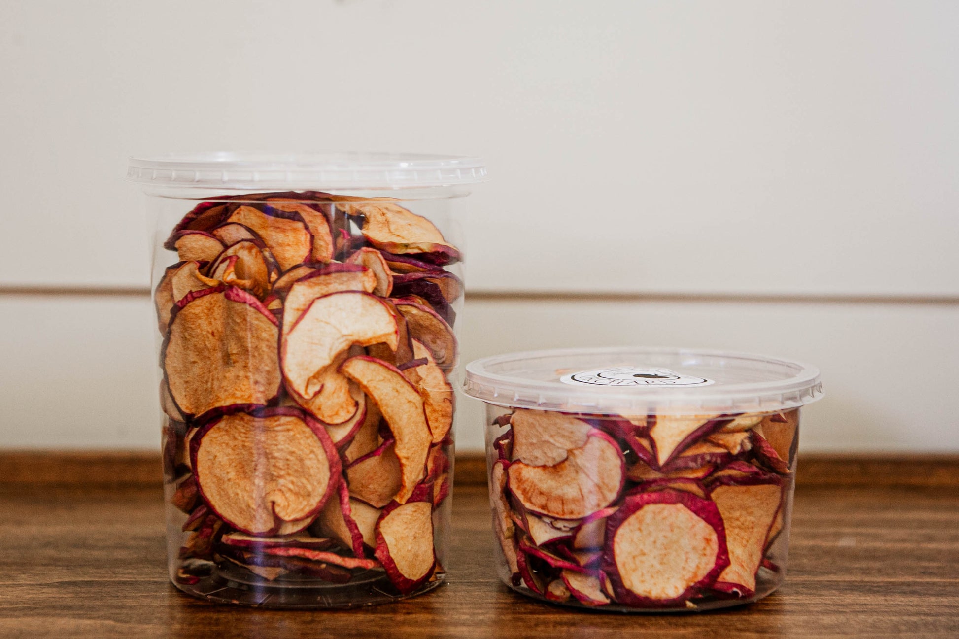 This image displays containers of apple chips, which appear to be a delicious and healthy snack option. The apple chips are neatly packaged in clear plastic tubs, allowing the viewer to see the crisp, evenly sliced apple pieces inside. Dried in the kitchen of Nystrom Orchard in Worthington Minnesota.