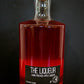 Bottle of pink liqueur in a glass bottle with a black lid on a black background. Hand crafted in the kitchen at Nystrom Orchard in Worthington Minnesota.