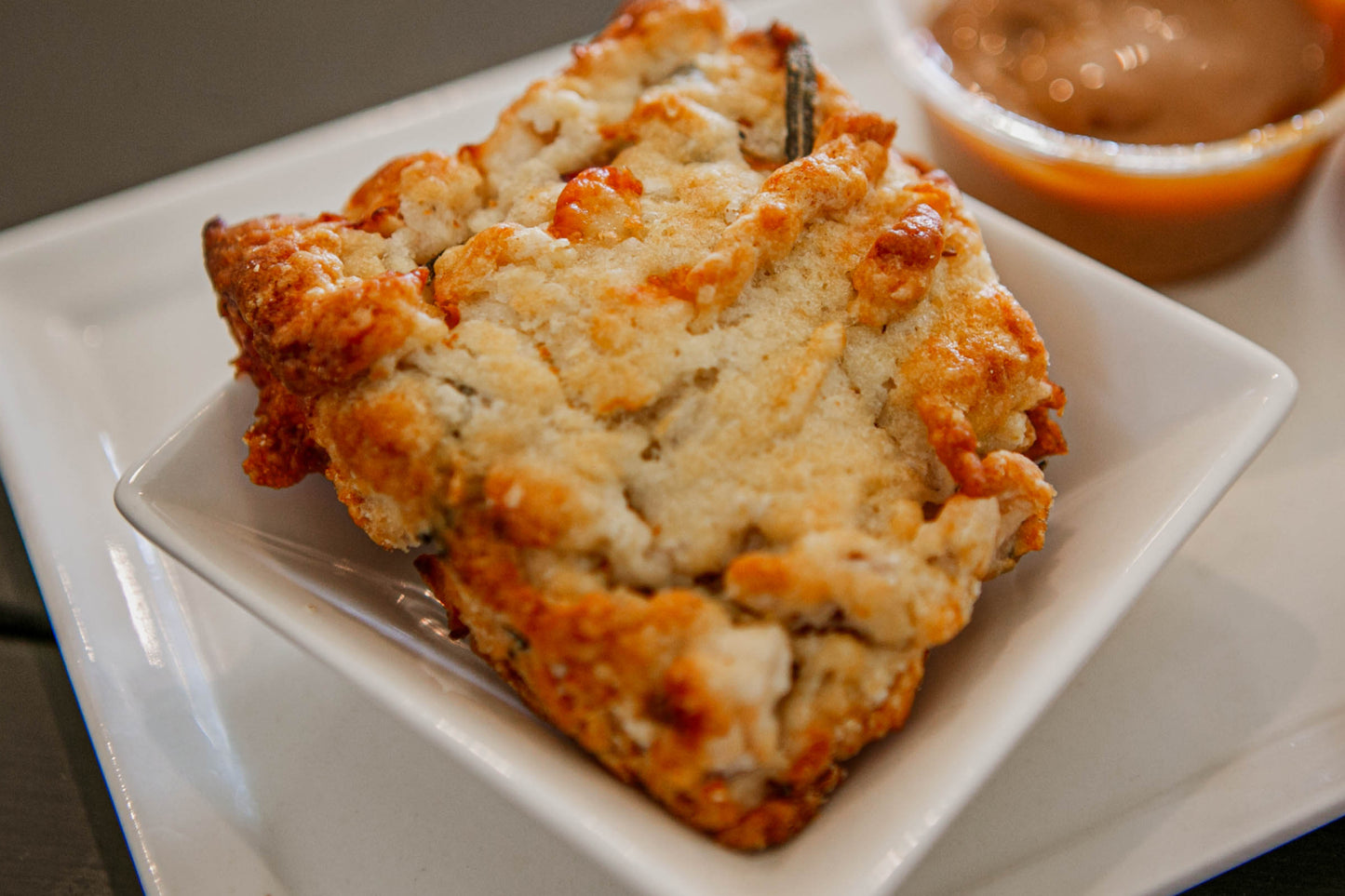 A photo of a single biscuit with cheddar cheese apples and herbs, placed on a white plate. Baked in the kitchen of Nystrom Orchard in Worthington Minnesota.