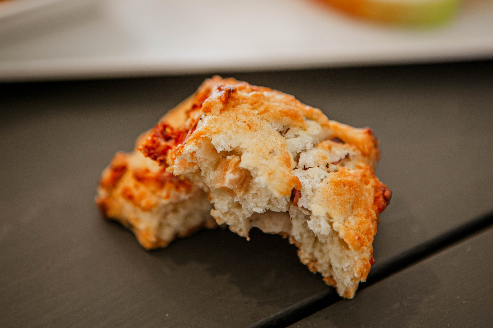 Apple cheddar rosemary biscuit broken in half on a dark surface with a blurry background. Baked in the kitchen of Nystrom Orchard in Worthington Minnesota.