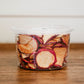 Container of dried apple chips on a wooden surface.  Dried in the kitchen of Nystrom Orchard in Worthington Minnesota.
