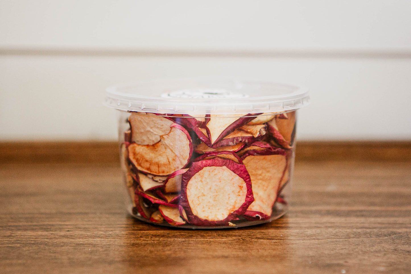Container of dried apple chips on a wooden surface.  Dried in the kitchen of Nystrom Orchard in Worthington Minnesota.